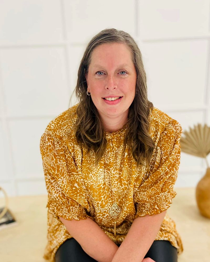 Molly Feit, founder of AM Financial Solutions, seated and smiling in a gold patterned top